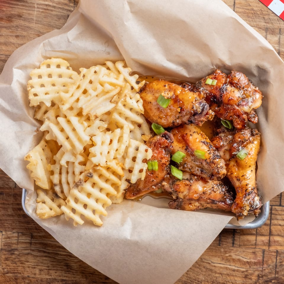 Crispy waffle fries and glazed chicken wings topped with green onions in a metal tray.
