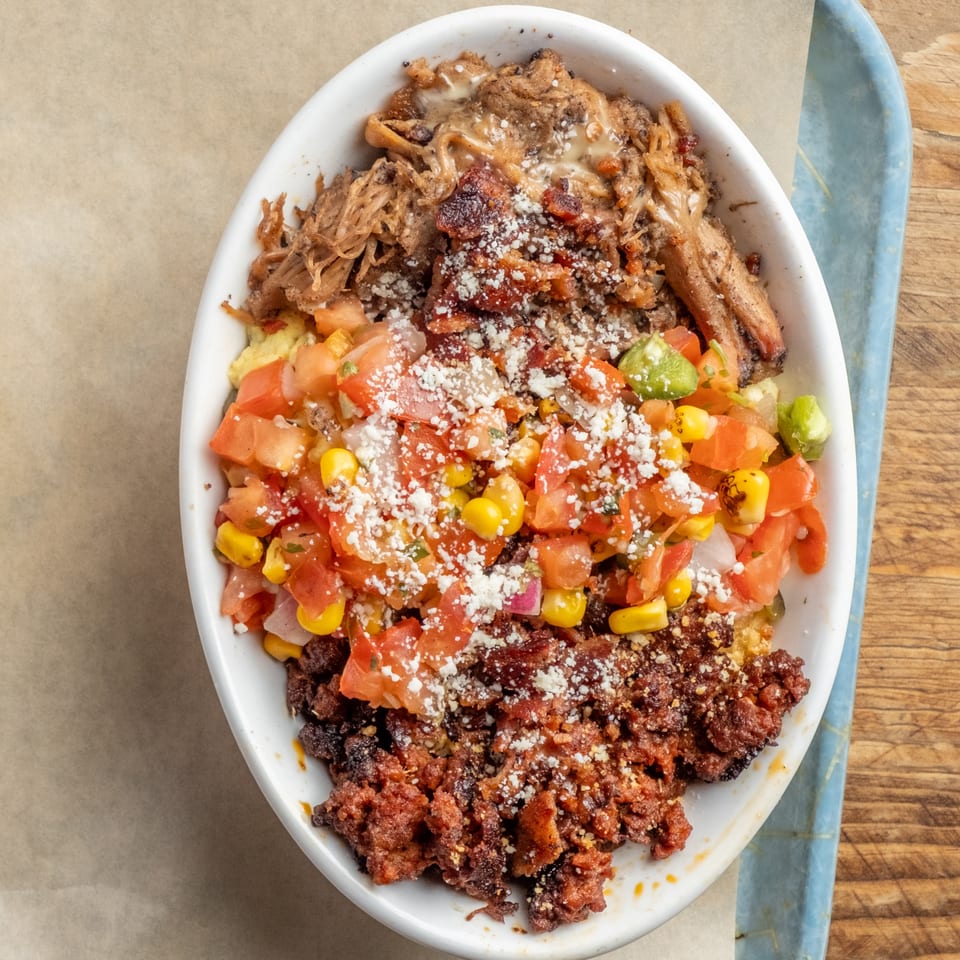Close-up of a white bowl filled with pulled pork, chorizo, corn, tomatoes, and cheese.
